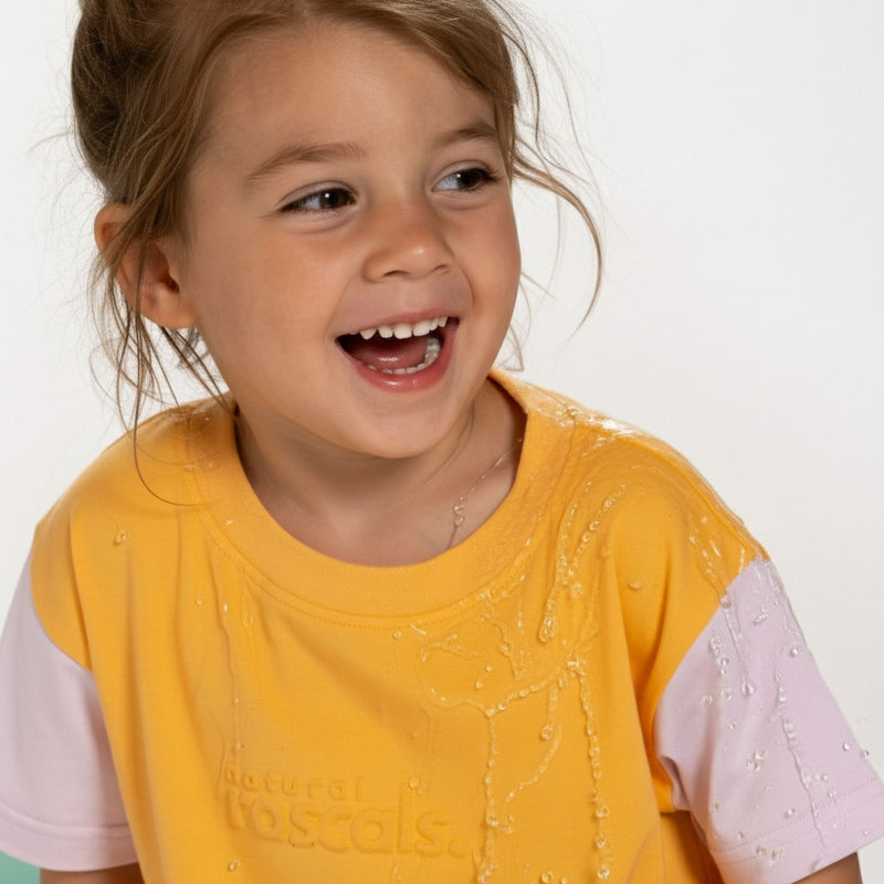 Child wearing an apricot organge and lavender spill resistant t shirt by Natural Rascals with 'Natural Rascals' branding on a white background