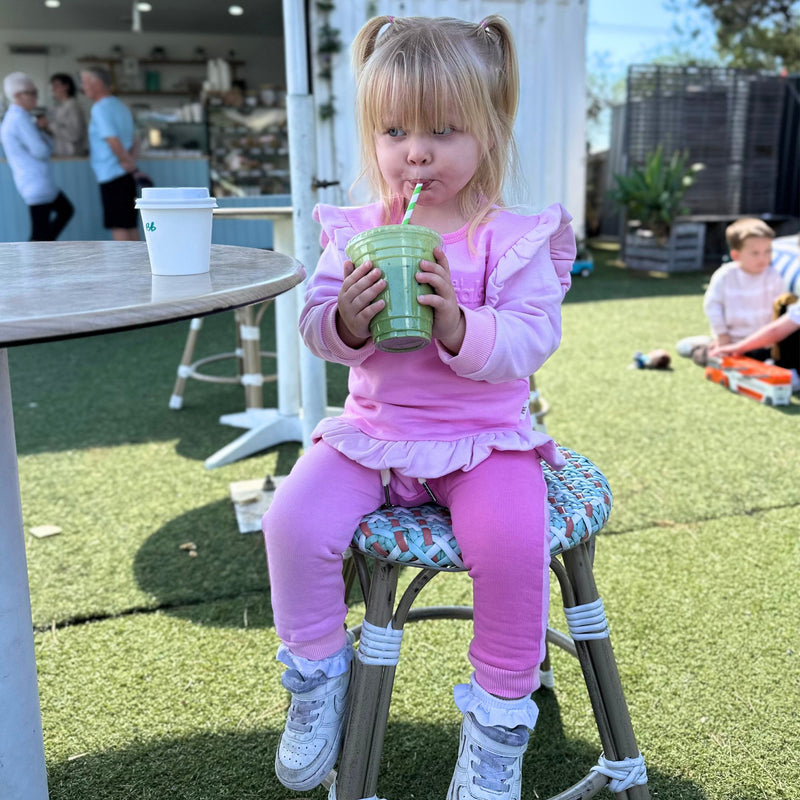 Child in raspberry and candy pink spill resistant outfit drinking from a green cup outdoors by Natural Rascals