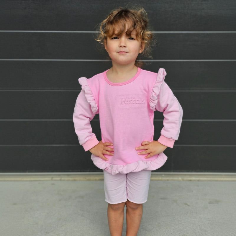 Young girl wearing a raspberry candy pink spill resistant outfit with ruffled sleeves against a dark wall by Natural RASCALS