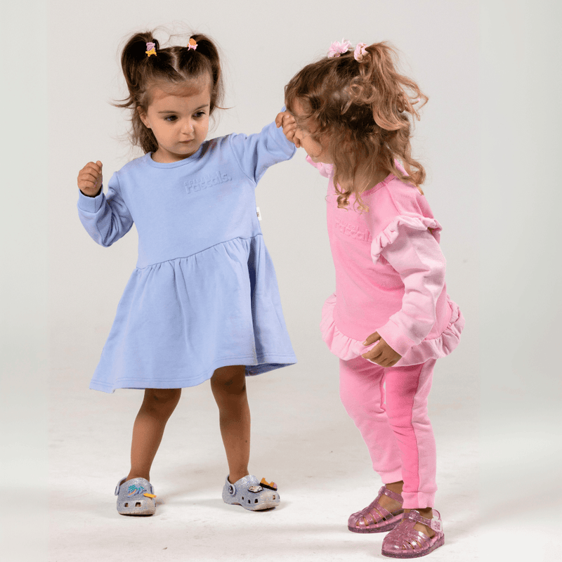 Two children holding hands wearing a Spill-Resistant Dress in Periwinkle Lavender and a set in raspberry and candy pink by Natural Rascals
