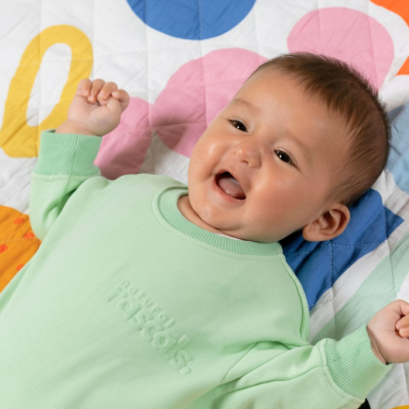 Up close image of Baby in light green spill-resistant onesie romper Natural Rascals on a playmat