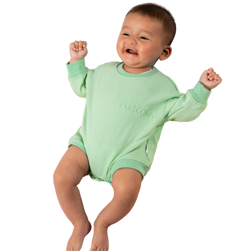 Baby in mint green spill-resistant onesie romper by Natural Rascals on transparent background.