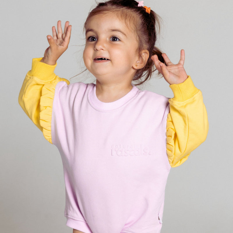 Happy child wearing a two tone pastel lavender, sunshine yellow spill resistant romper by Natural Rascals with a gray background