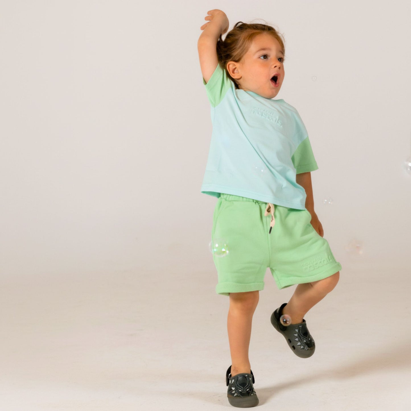 Happy child jumping in excitement wearing mint green and matching airy blue and mint green spill resistant t shirt by Natural Rascals