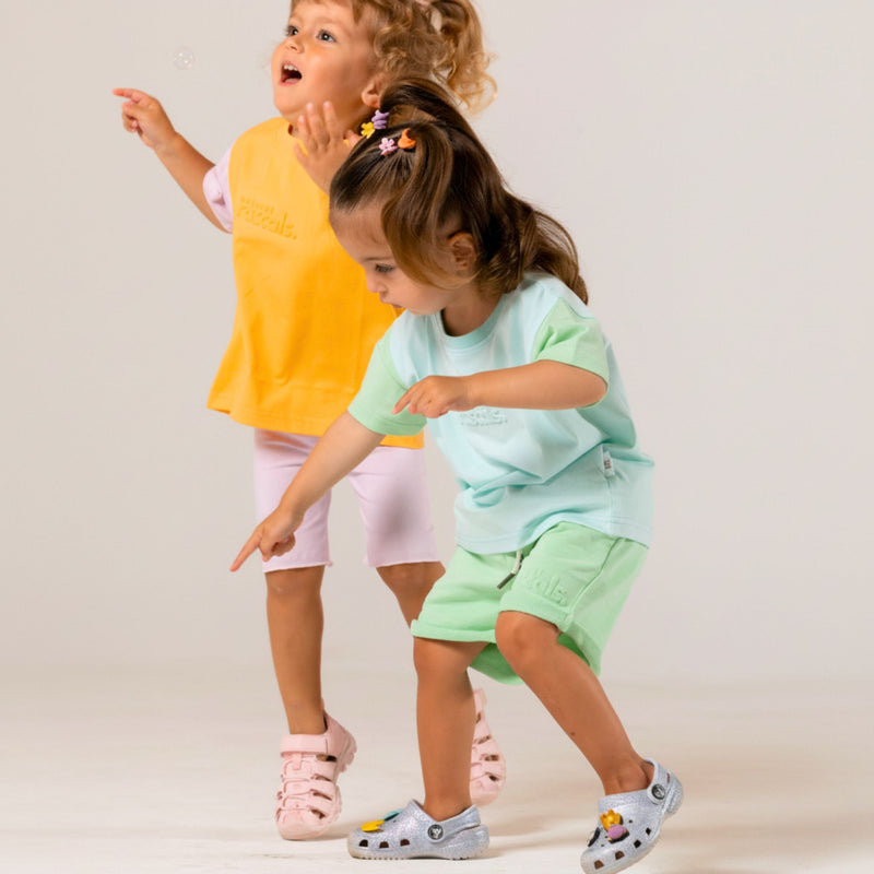 Two children playing in gender-neutral mint green and apricot orange spill-resistant baby toddler tees and shorts by Natural Rascals.