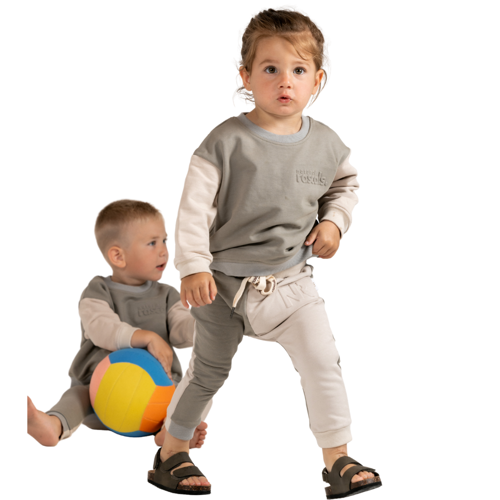 Children in grey and light beige spill-resistant baby toddler set by Natural Rascals on transparent background