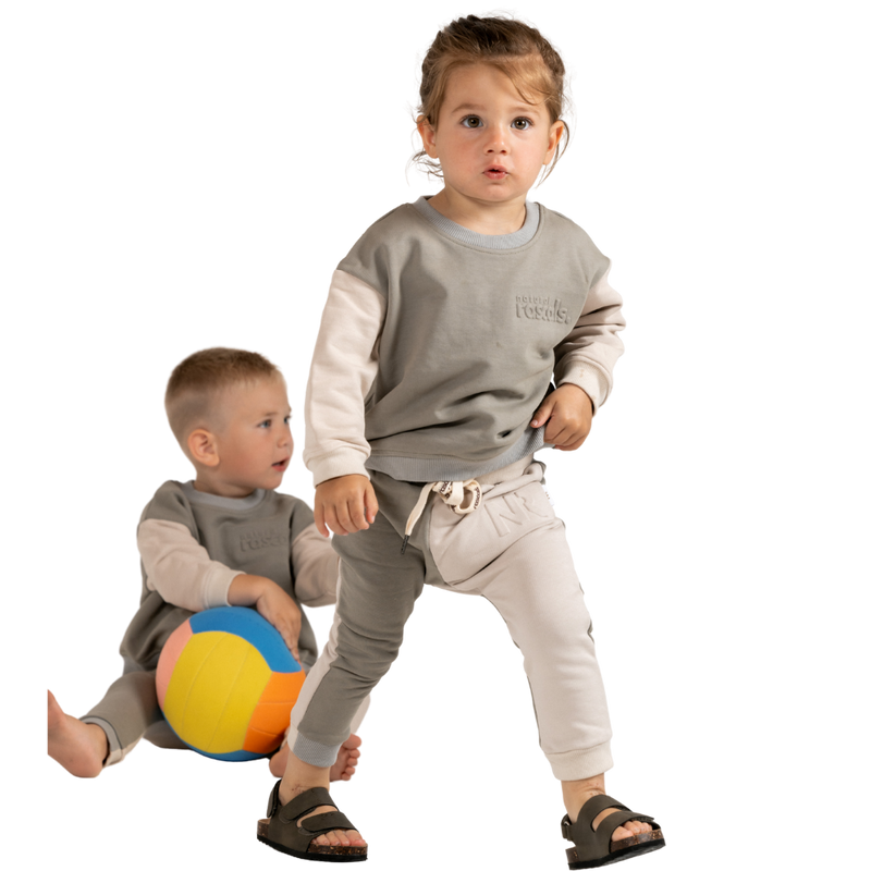 Children in grey and light beige spill-resistant baby toddler set by Natural Rascals on transparent background