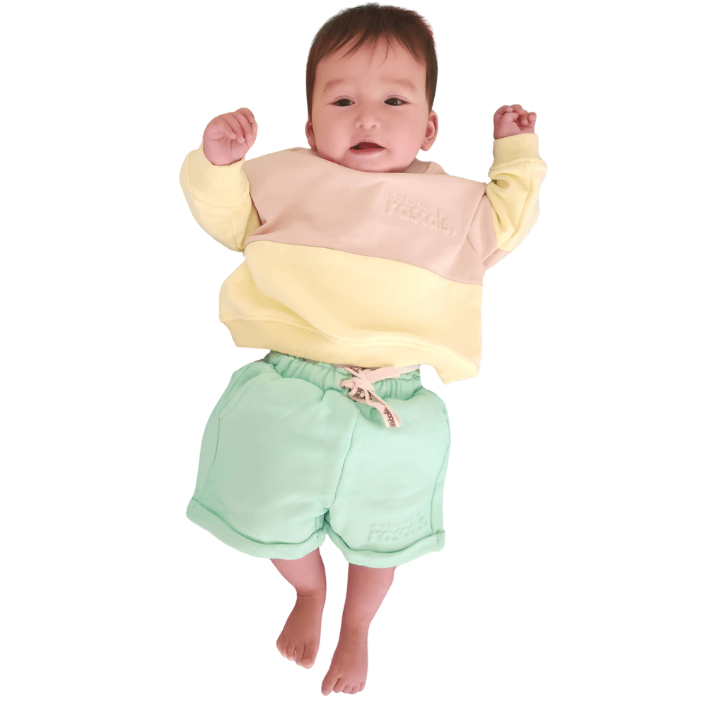 Baby wearing a lemonade yellow, oat and mint green Spill resistant shorts and sweat set by Natural Rascals on a transparent background