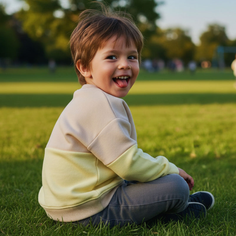 Child sitting on grass in a park with a blurred background wearing a spill resistant sweat lemonade and oat sweat by Natural Rascals