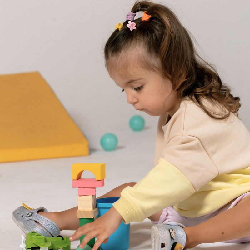 Child playing with colorful building blocks on a light surface wearing a spill resistant gender neutral spill resistant sweat in lemonade yellow and oat by Natural Rascals