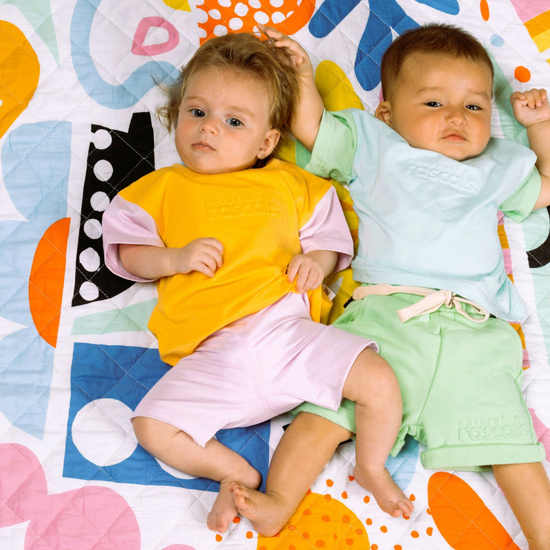 Babies relaxing in apricot orange and soft lilac spill-resistant baby toddler tees by Natural Rascals.